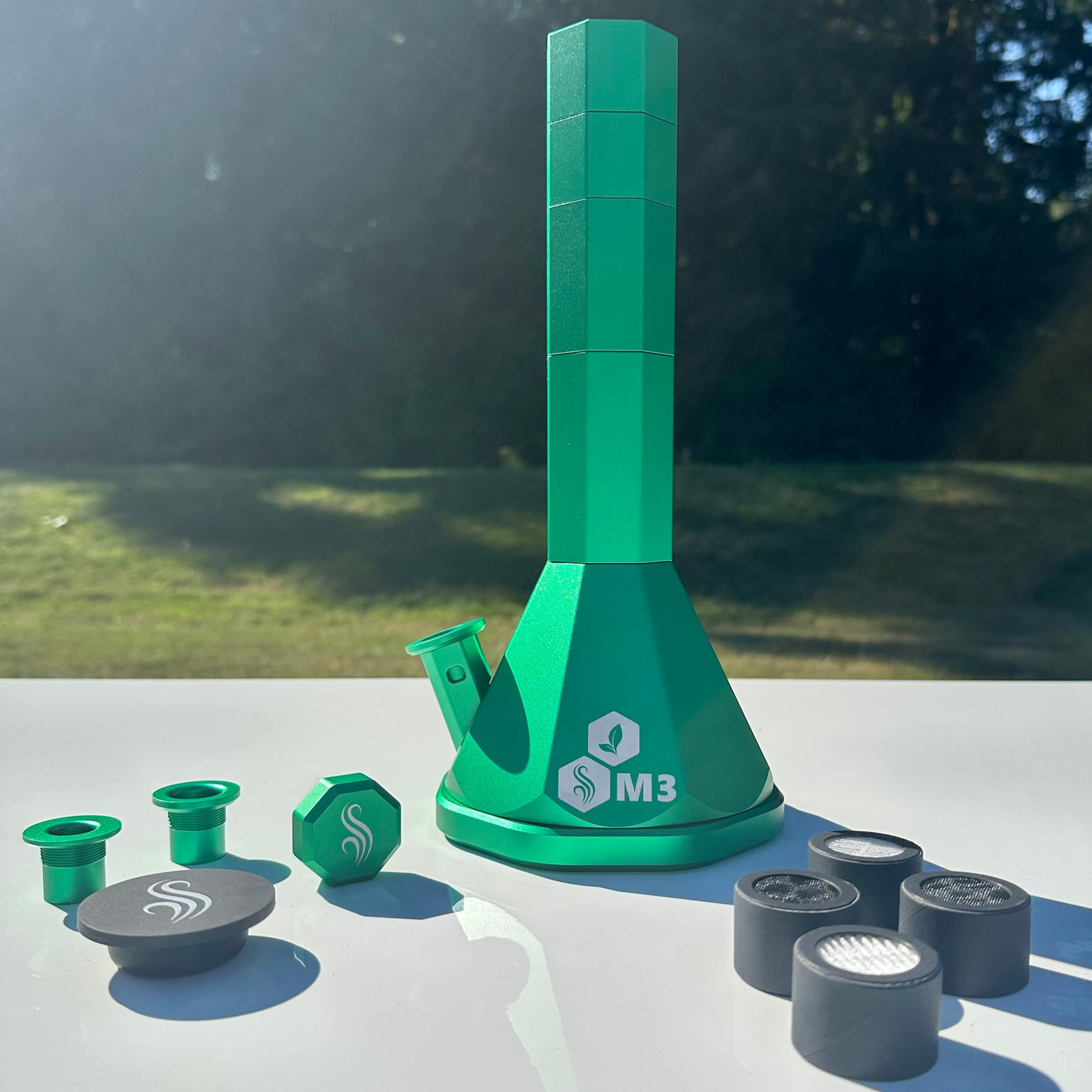 Green M3 bong with accessories and 4 filters on a white surface outdoors