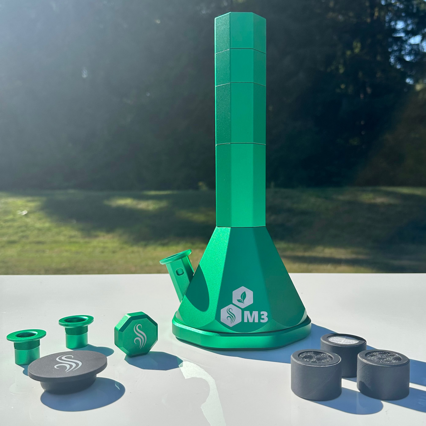 Green M3 bong with accessories and 3 filters on a white surface outdoors